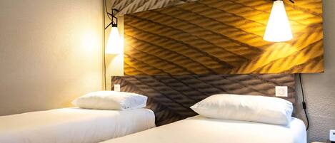 A hotel room with two beds, a textured wall, and pendant lights.
