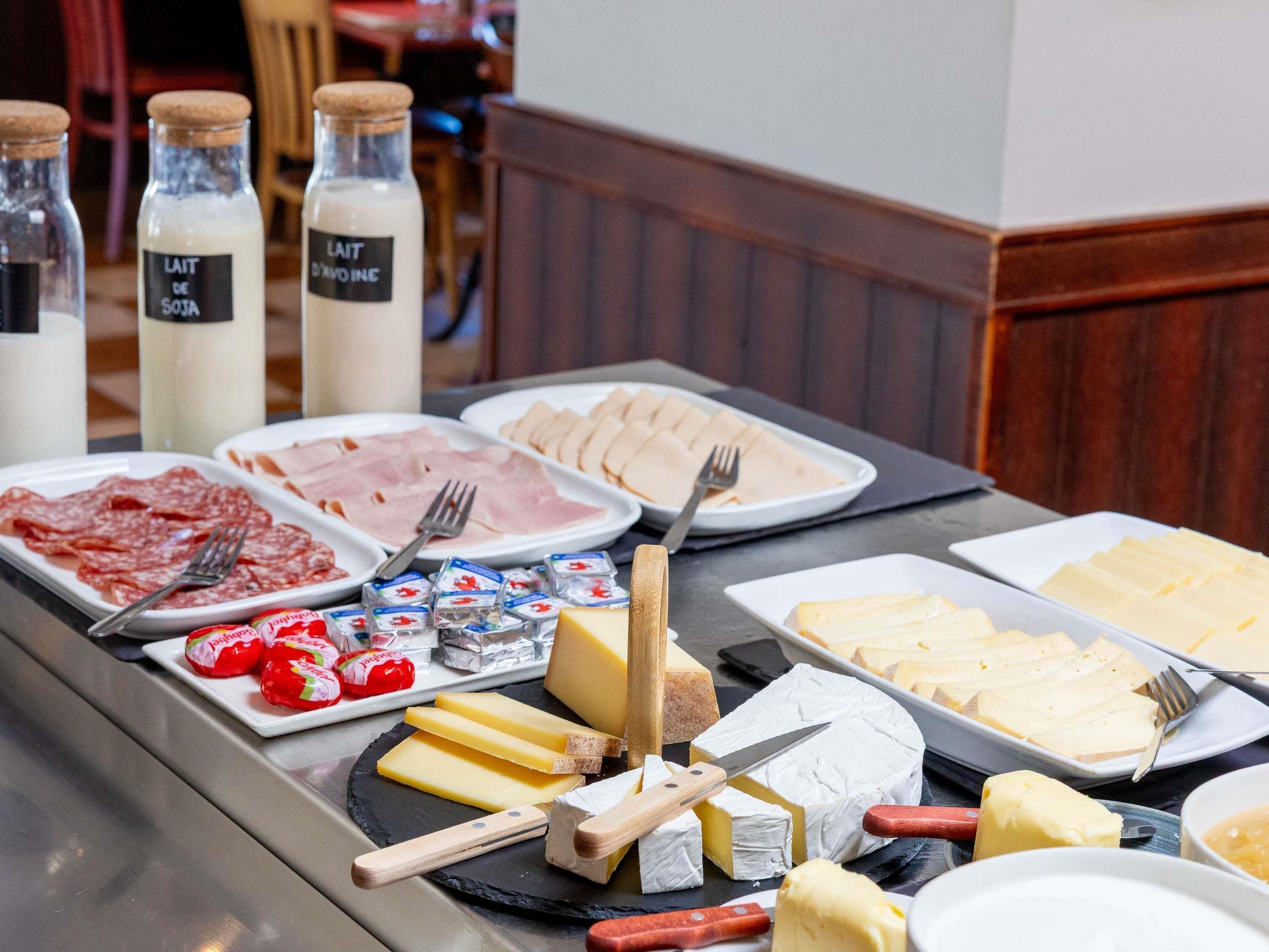 A buffet with various cheeses, meats, and condiments.