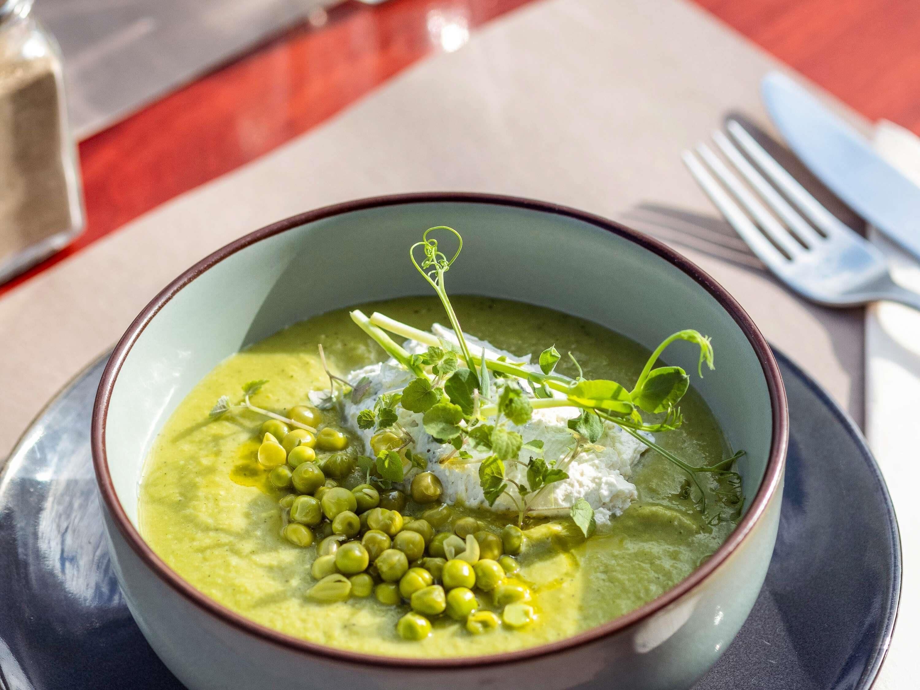 A bowl of green soup with peas and herbs on a plate.