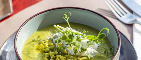 A bowl of green soup with peas and herbs on a plate.