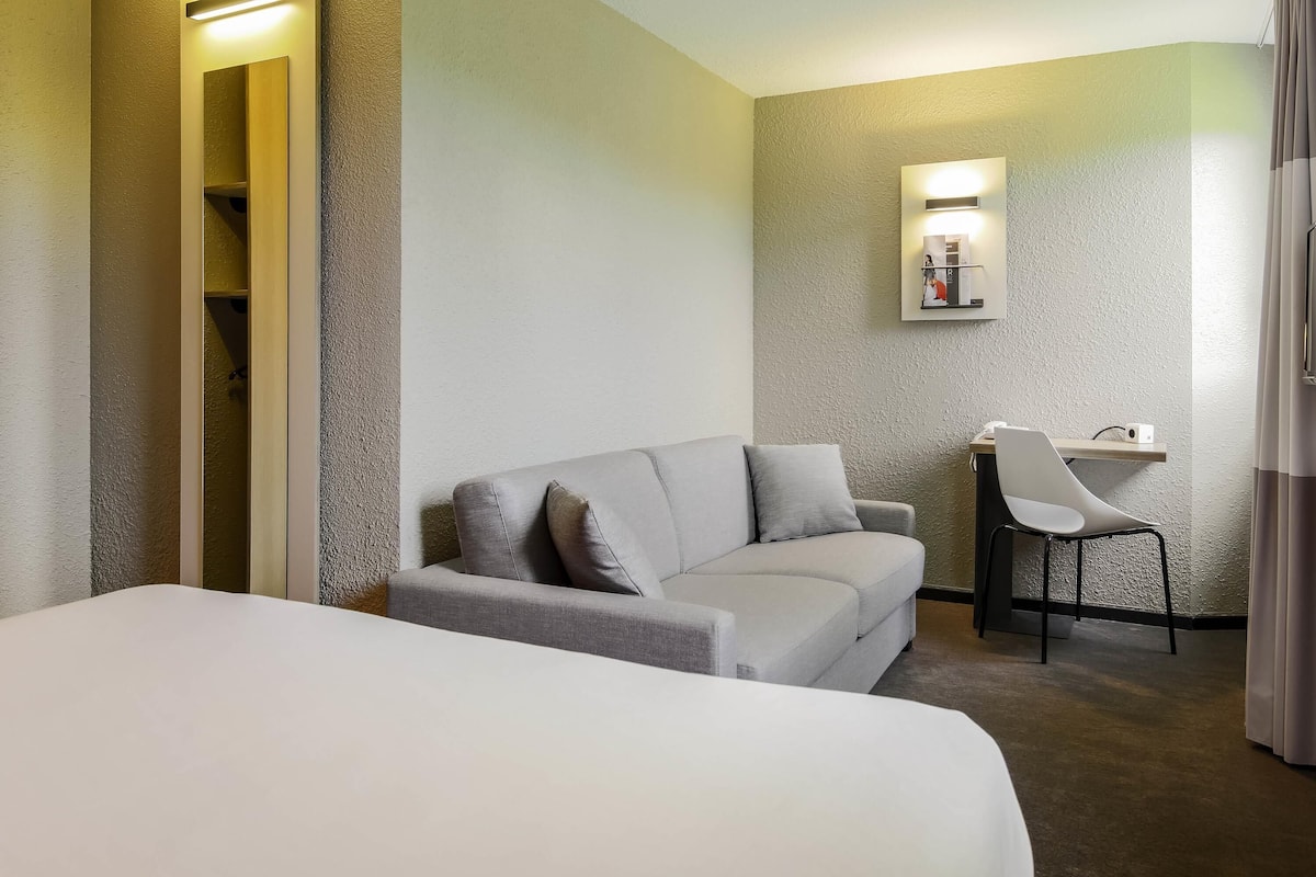 Une chambre d’hôtel comprenant un lit, un canapé, un bureau avec une chaise et une petite table avec une lampe.