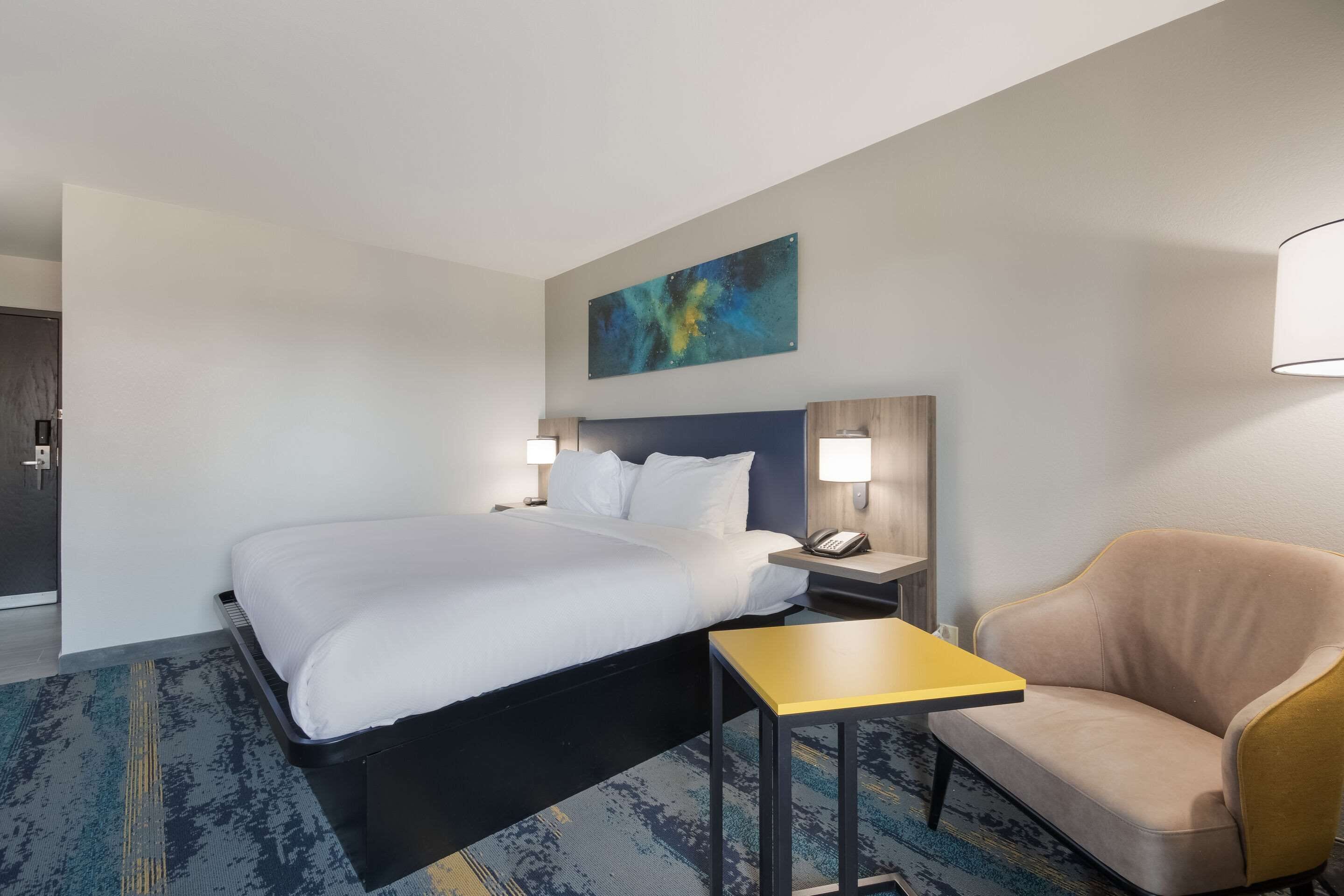 A hotel room with a bed, bedside tables, a lamp, a sofa, and a painting on the wall.