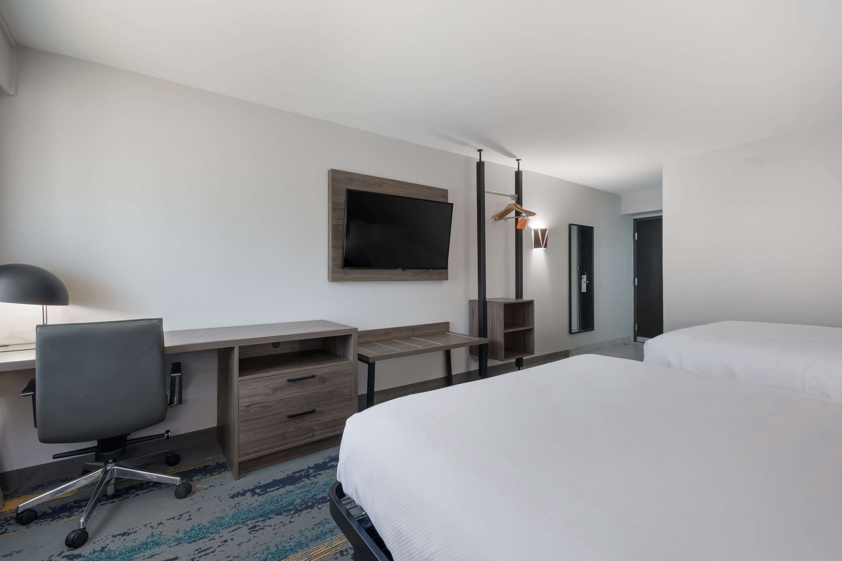 A hotel room with a bed, a desk with a chair, a TV mounted on the wall, and a wardrobe.