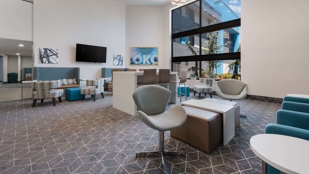 A modern lobby with a reception desk, seating area, and large windows offering a view of the outdoors. - Clarion Pointe OKC Airport (Oklahoma City)