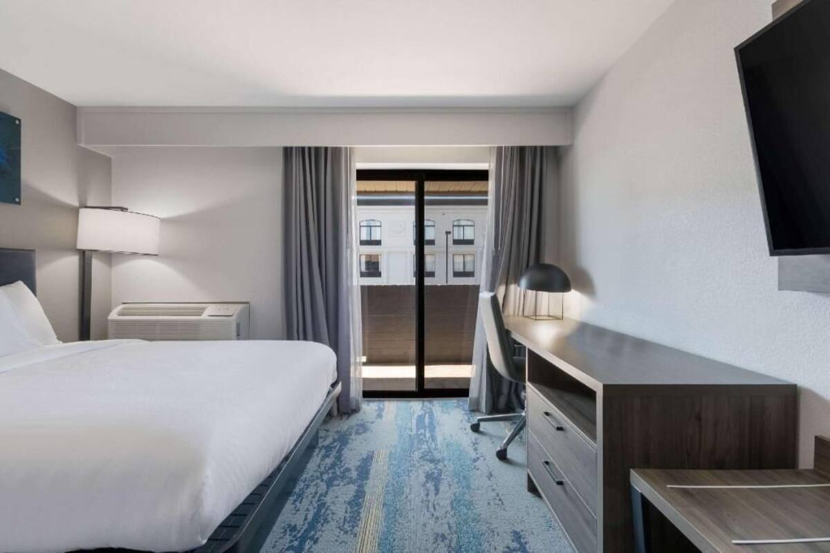 Habitación de hotel con cama, escritorio, silla y un amplio ventanal con cortinas.