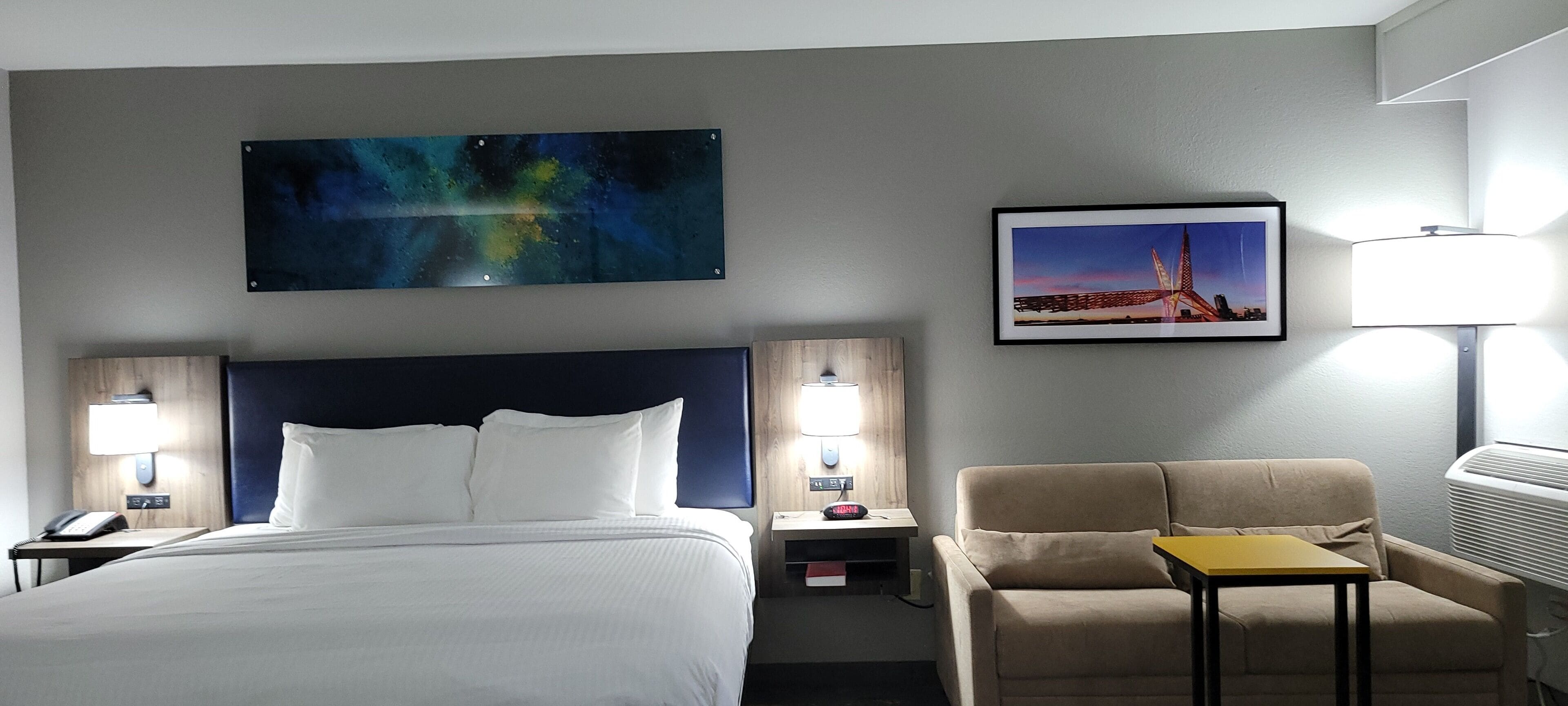 A hotel room with a bed, a desk, a chair, a lamp, and two wall-mounted lamps.