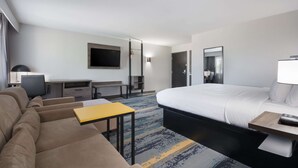 A hotel room with a bed, a sofa, a desk, and a TV. - Clarion Pointe OKC Airport (Oklahoma City)
