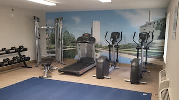 Un gimnasio con máquinas de cardio, mancuernas y una colchoneta azul.