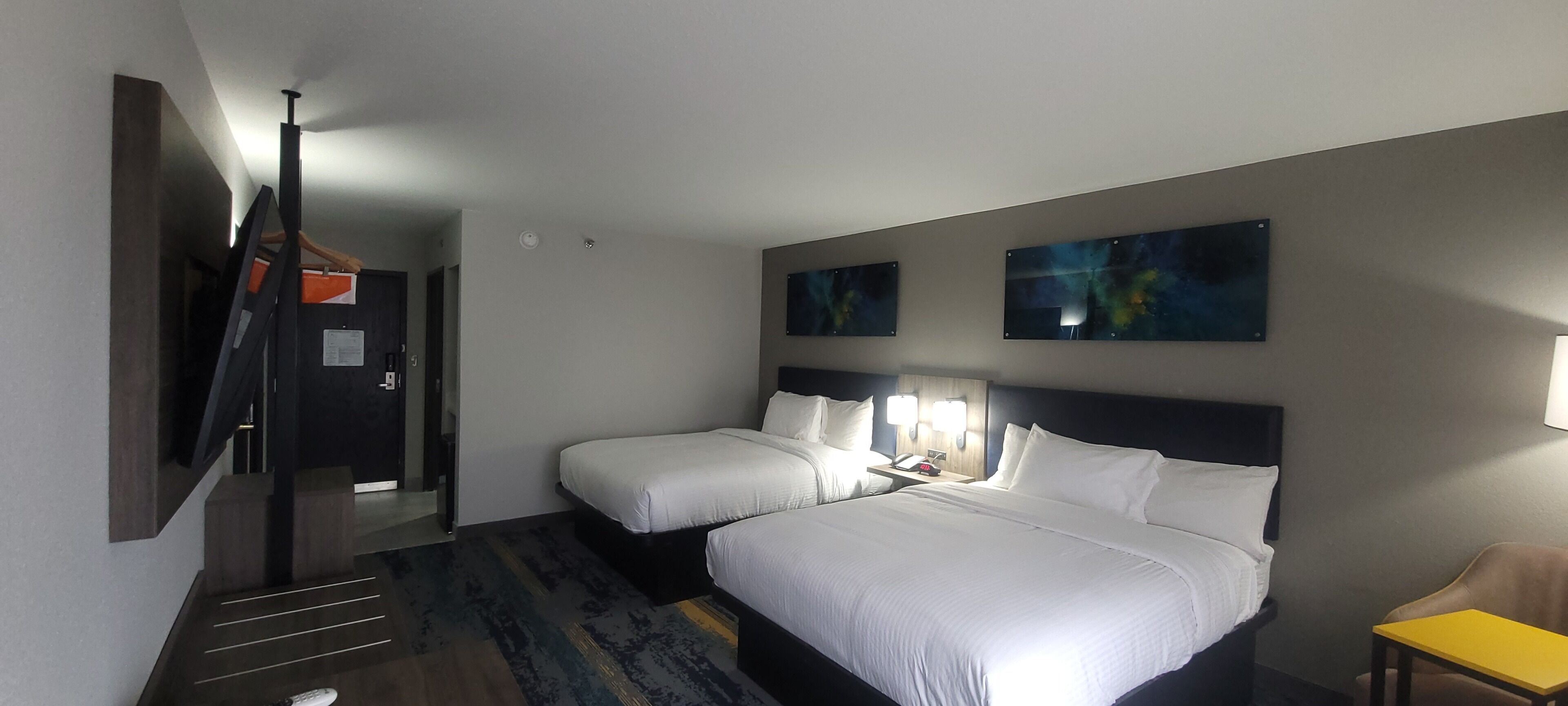 A hotel room with two beds, a TV, a desk, and artwork on the walls.
