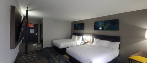 A hotel room with two beds, a TV, a desk, and artwork on the walls.