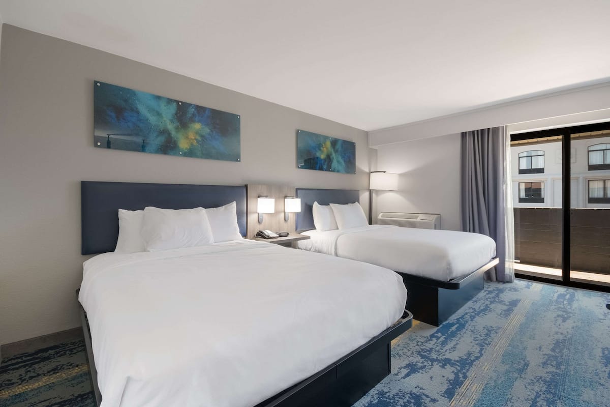 Una habitación de hotel con dos camas, un ventanal con vistas y una obra de arte abstracta en la pared.