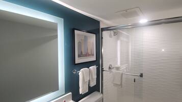 A modern bathroom with a glass shower enclosure, a framed cityscape picture on the wall, and a towel rack with two white towels.