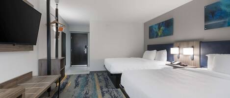 A hotel room with two beds, a flat-screen TV, a desk, and a door leading to a hallway.