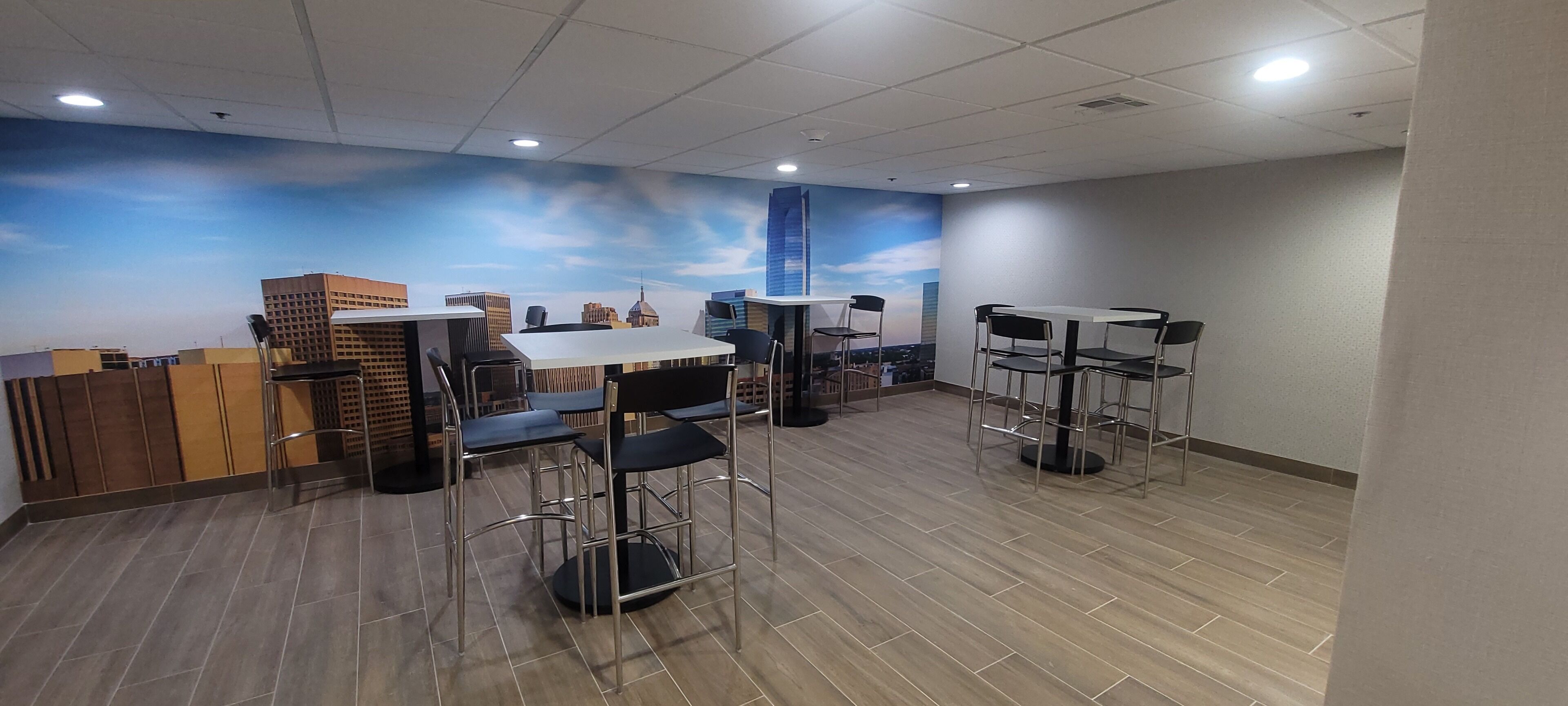 A modern indoor space with a cityscape mural on the wall, multiple tables and chairs, and a wooden floor.