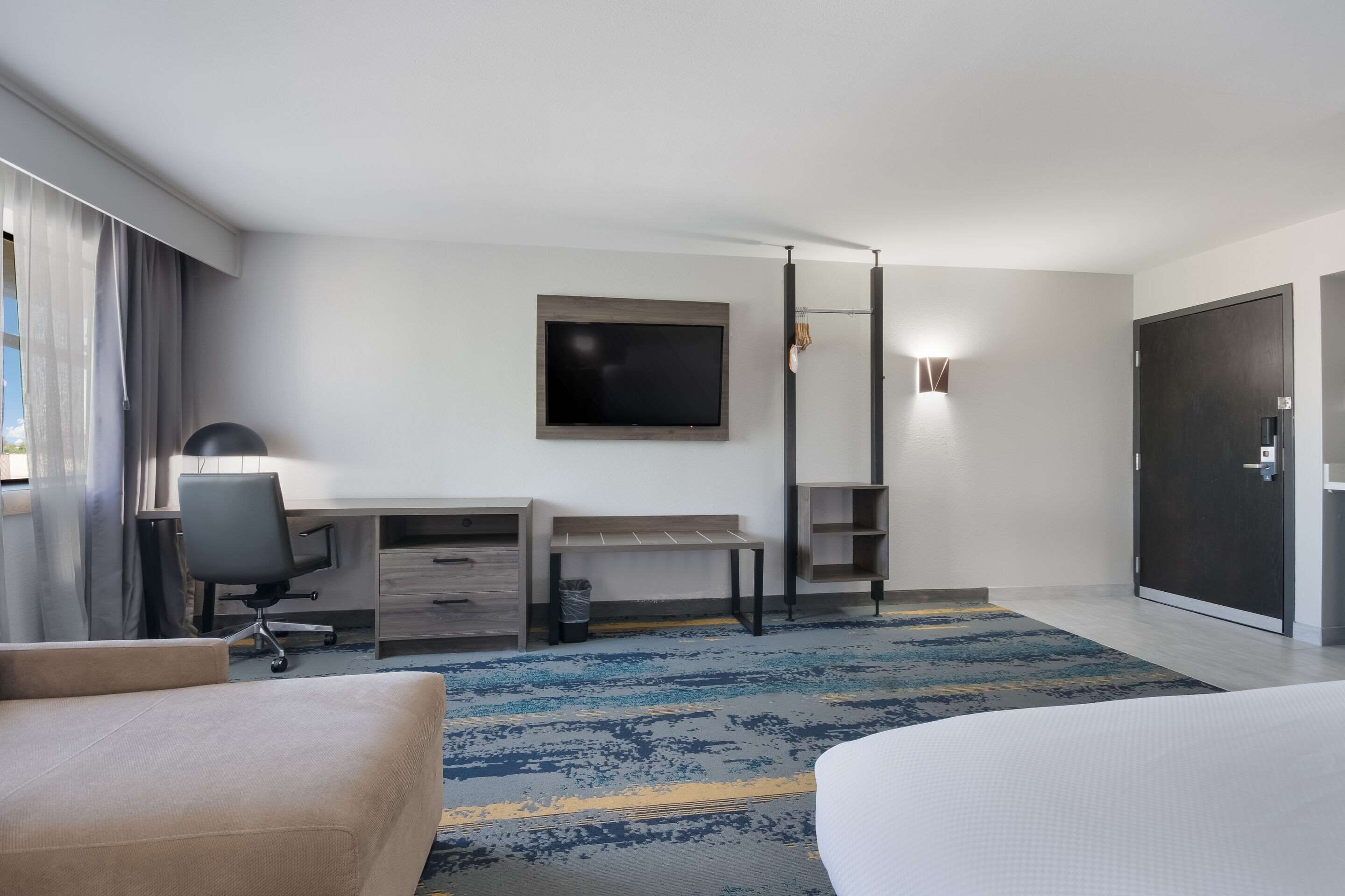 A hotel room with a bed, a desk with a chair, a television, and a door.