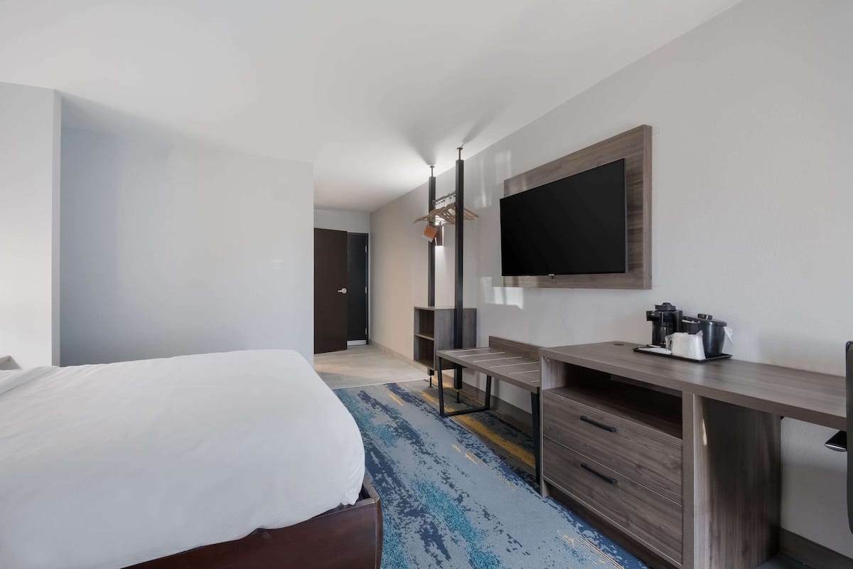 Una habitación de hotel moderna con una cama grande, un escritorio con televisión de pantalla plana y una cafetera.