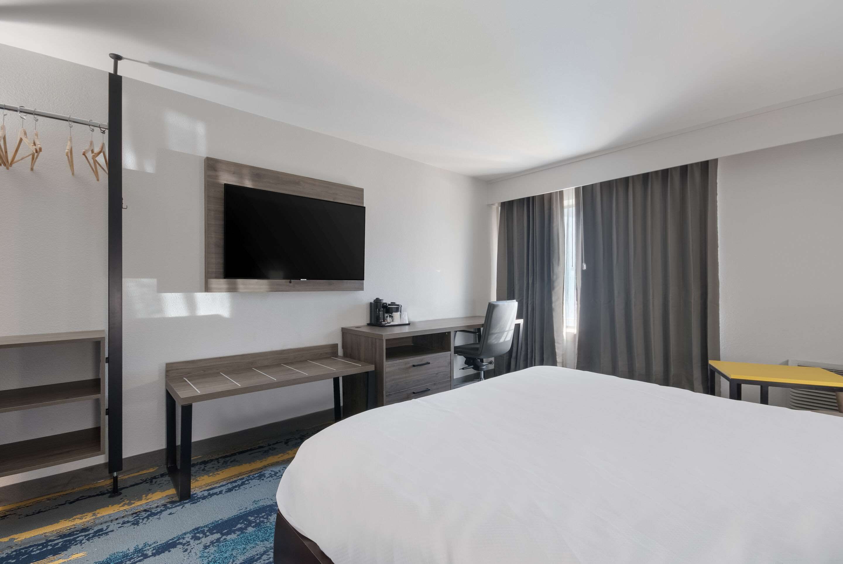 Une chambre d’hôtel avec un lit, un bureau, une chaise, une télévision et une fenêtre avec des rideaux.
