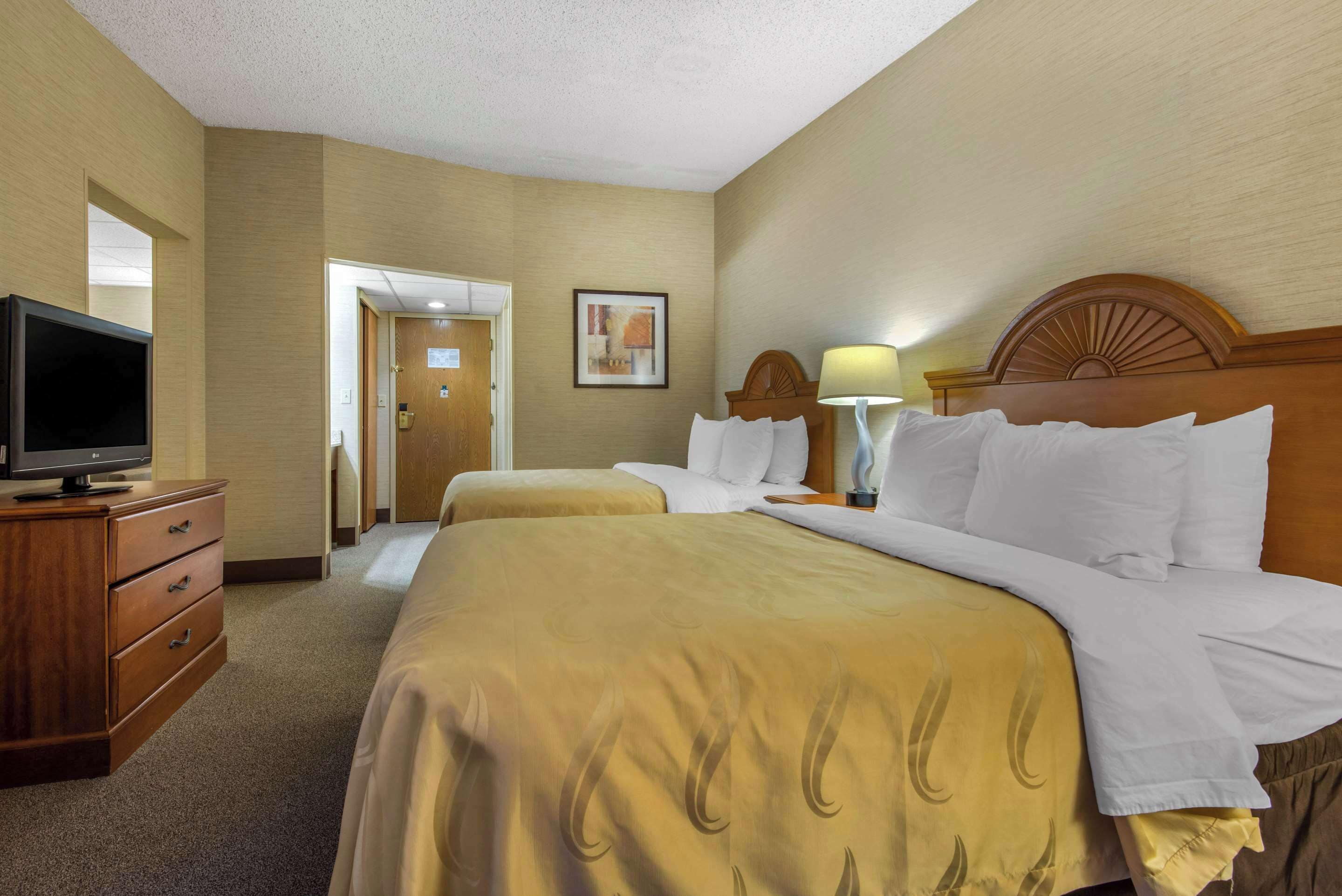 A hotel room with a large bed, a television on a wooden dresser, and a door leading to another room.
