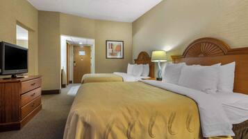 Una habitación de hotel con una cama grande, un televisor sobre un aparador de madera y una puerta que da a otra habitación.