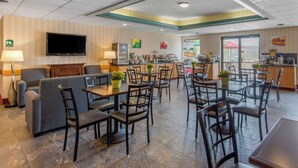 A hotel dining area with multiple tables and chairs, a sofa, a television, and a buffet counter. - Quality Inn & Suites Mansfield (Mansfield)