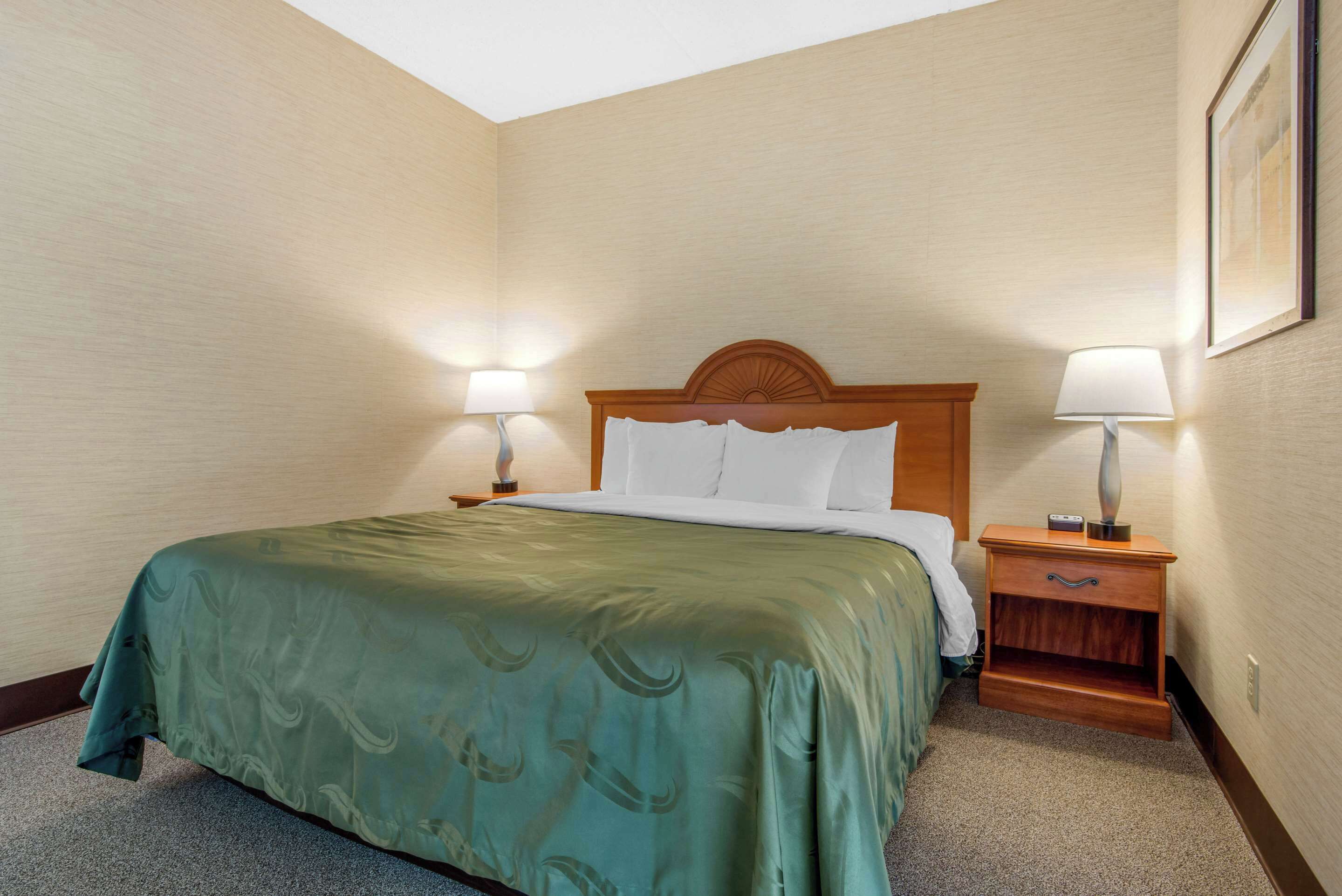 A hotel room with a bed, two bedside tables with lamps, a nightstand, and a framed picture on the wall.
