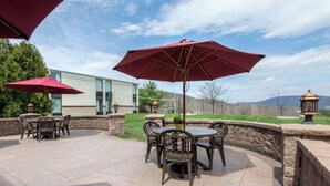 An outdoor patio area with stone flooring, a round table with chairs, and two red umbrellas. - Quality Inn & Suites Mansfield (Mansfield)