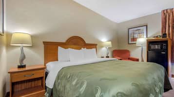 Habitación de hotel con una cama grande, dos mesitas de noche con lámparas, un sillón pequeño, un refrigerador y un cuadro en la pared.