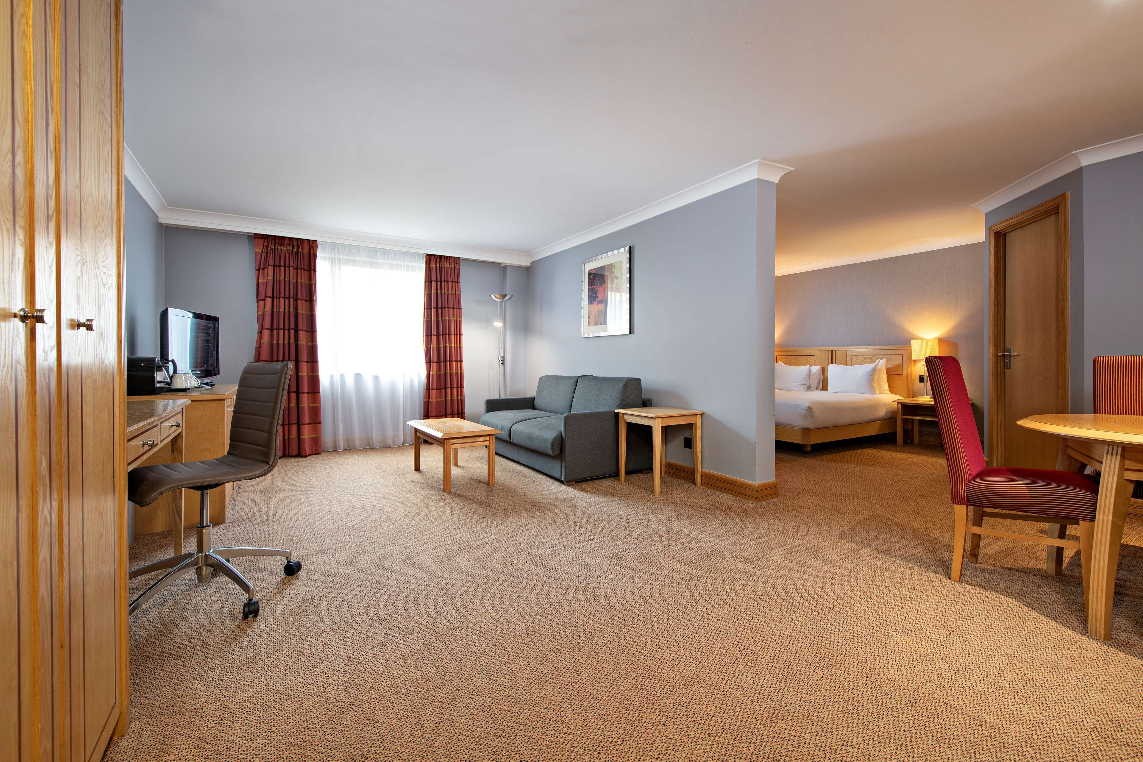 A hotel room with a desk, a sofa, a bed, a small table, and a chair.