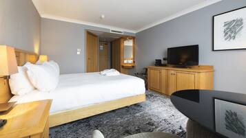 Habitación de hotel con cama, mesita de noche, televisor, armario de madera y un escritorio con silla.