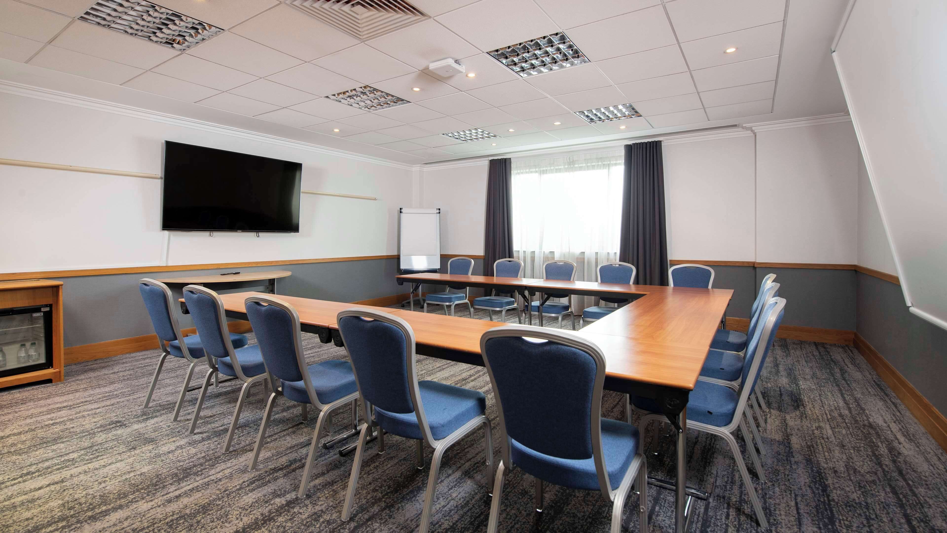 A conference room with a large table, blue chairs, a flat-screen TV, a whiteboard, and a projector screen.
