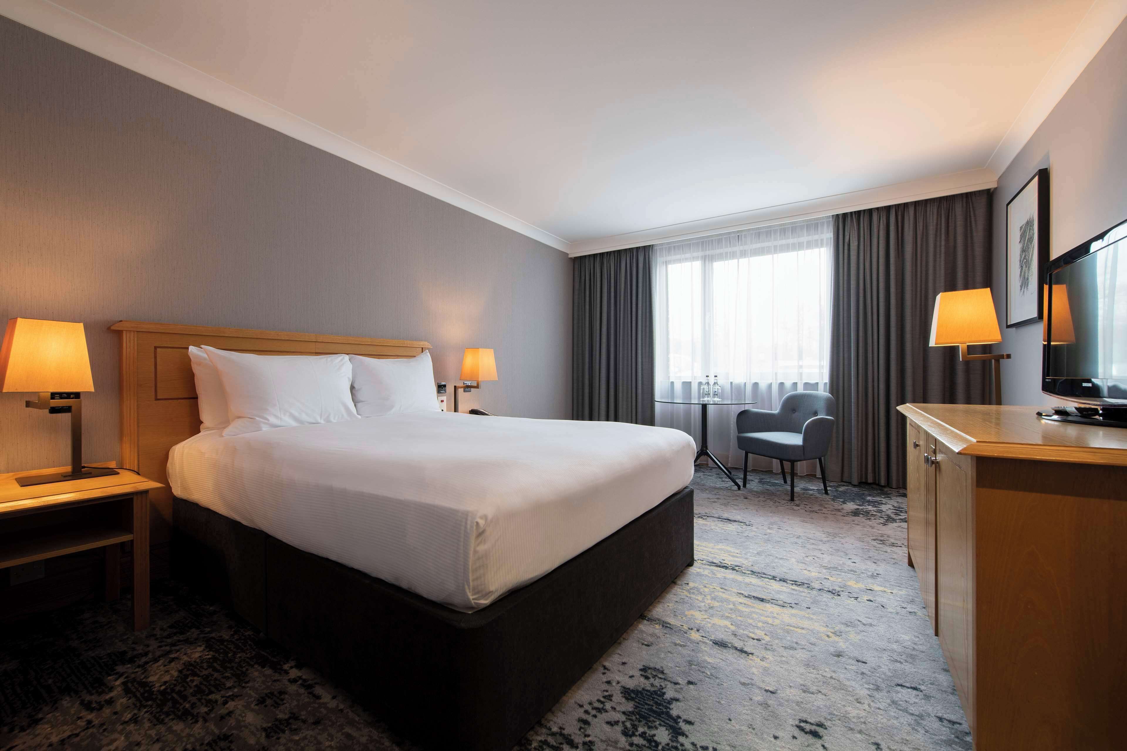 Habitación de hotel con una cama grande, dos lámparas de noche, un escritorio con una silla, un televisor y una ventana con cortinas.