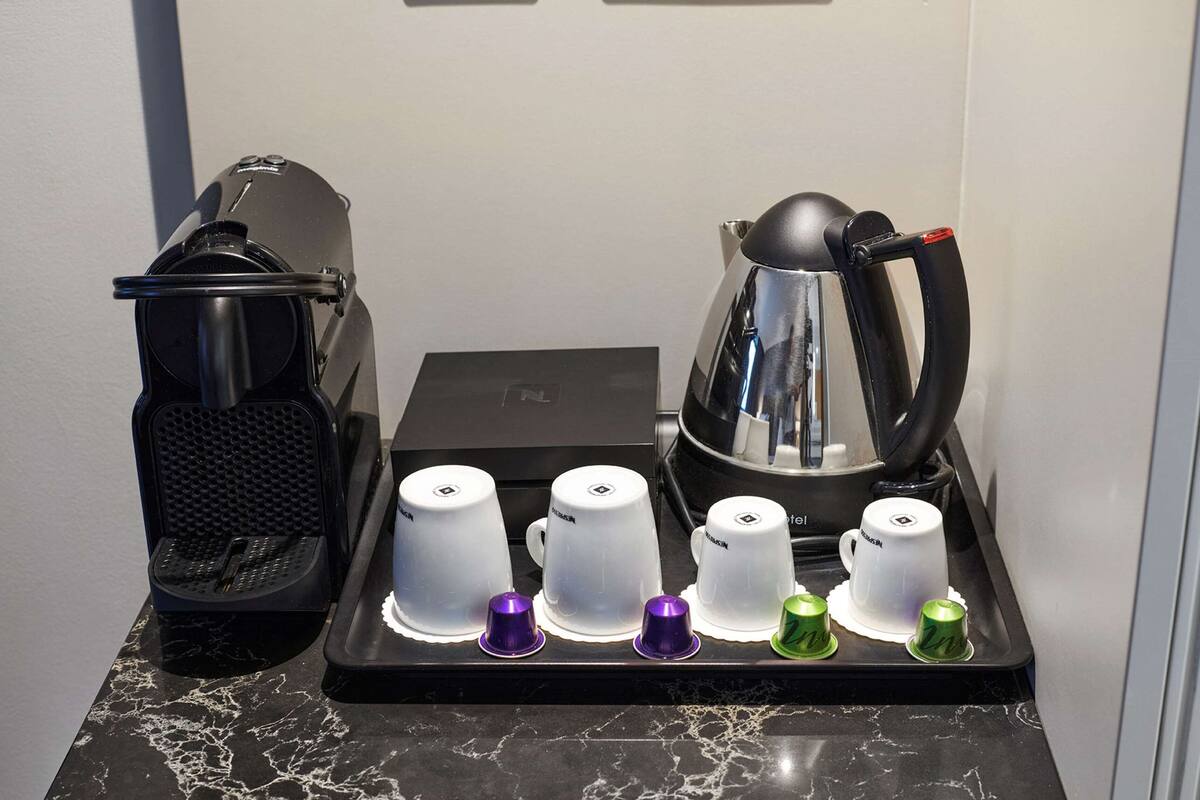 A coffee station with a coffee maker, several white cups, and a tray with colored lids.