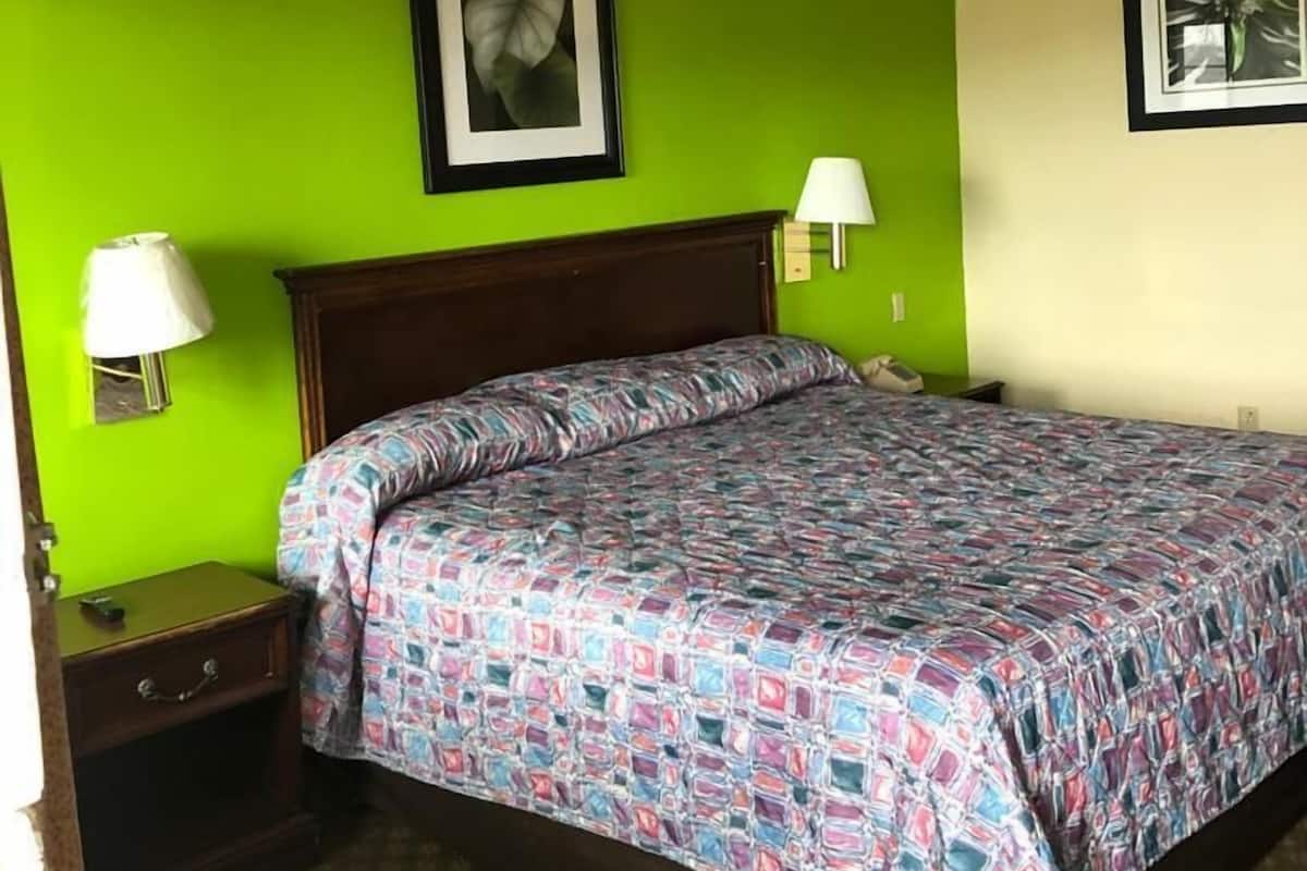 A hotel room with a bed, green walls, a framed picture, a bedside lamp, and a nightstand.