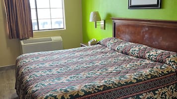 A hotel room with a bed, a nightstand, a lamp, a framed picture on the wall, and a window with curtains.