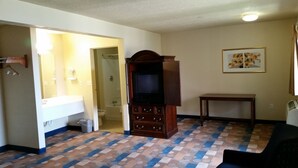 A living room with a patterned carpet, a television cabinet, a small table, and a framed picture on the wall. - Travel Inn Motel (Hartford)