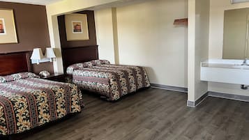 A hotel room with two beds, a bedside table with a lamp, a mirror, and a bathroom with a sink.