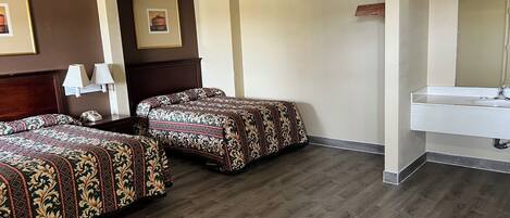 A hotel room with two beds, a bedside table with a lamp, a mirror, and a bathroom with a sink.