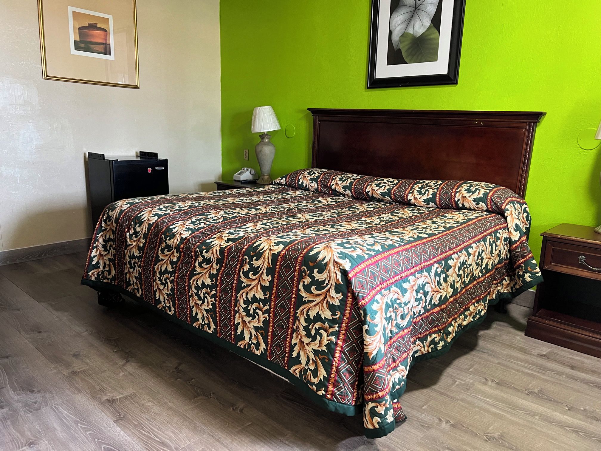 A hotel room with a large bed, a wooden headboard, a nightstand, a lamp, and a framed picture on the wall.