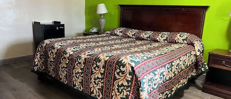 A hotel room with a large bed, a wooden headboard, a nightstand, a lamp, and a framed picture on the wall.