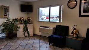 A reception area with a tiled floor, a flat-screen TV mounted on the wall, a window with a view of the street, and a clock on the wall. - Travel Inn Motel (Hartford)