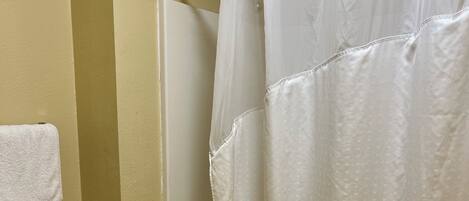 Un baño con inodoro blanco, bañera con cortina de ducha blanca y una toalla en el suelo.