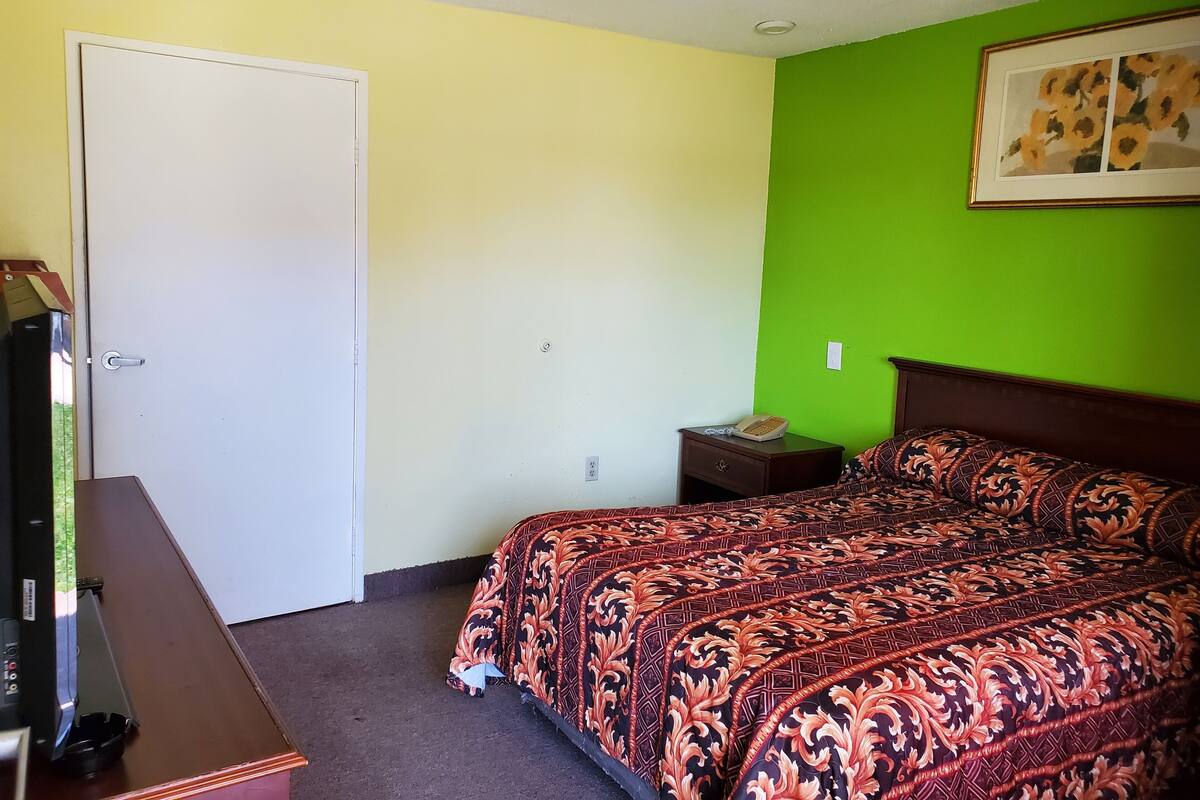 A room with a bed, a desk, a chair, a telephone, and a door.