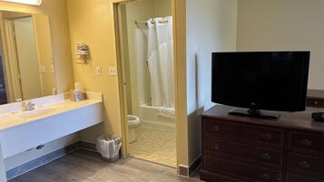 A bathroom with a sink, toilet, shower, and a television on a dresser.