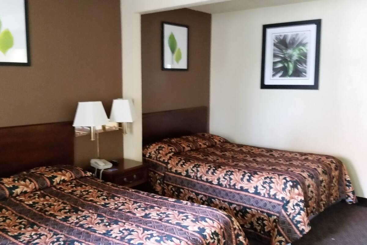 A hotel room with two beds, a nightstand with a lamp, and framed artwork on the walls.
