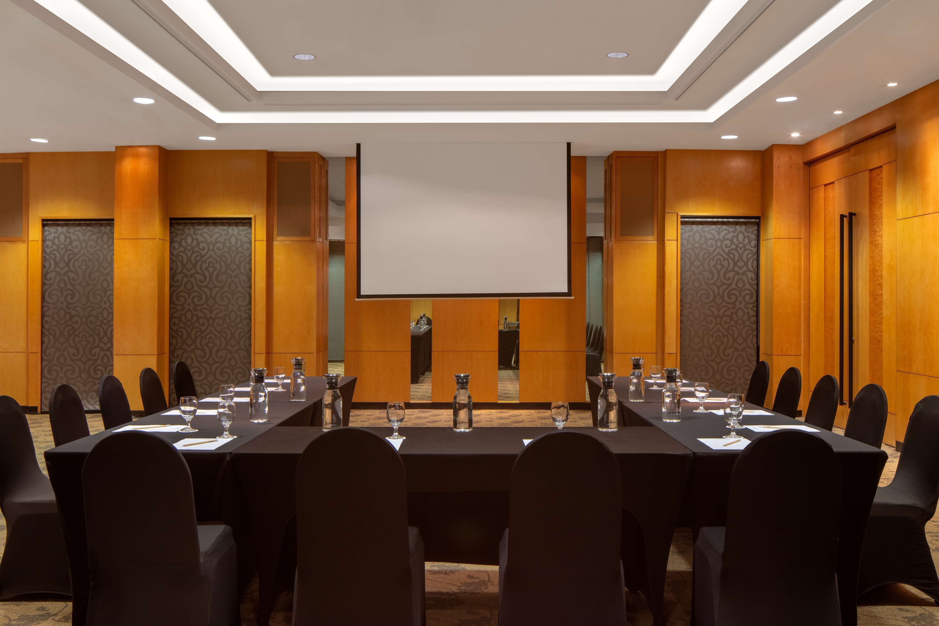 A conference room with a long table, chairs, a projector screen, and a carpeted floor.