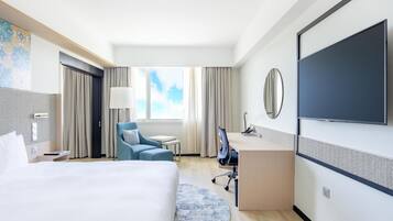 Habitación de hotel con cama, escritorio, silla, televisor y ventana con cortinas.