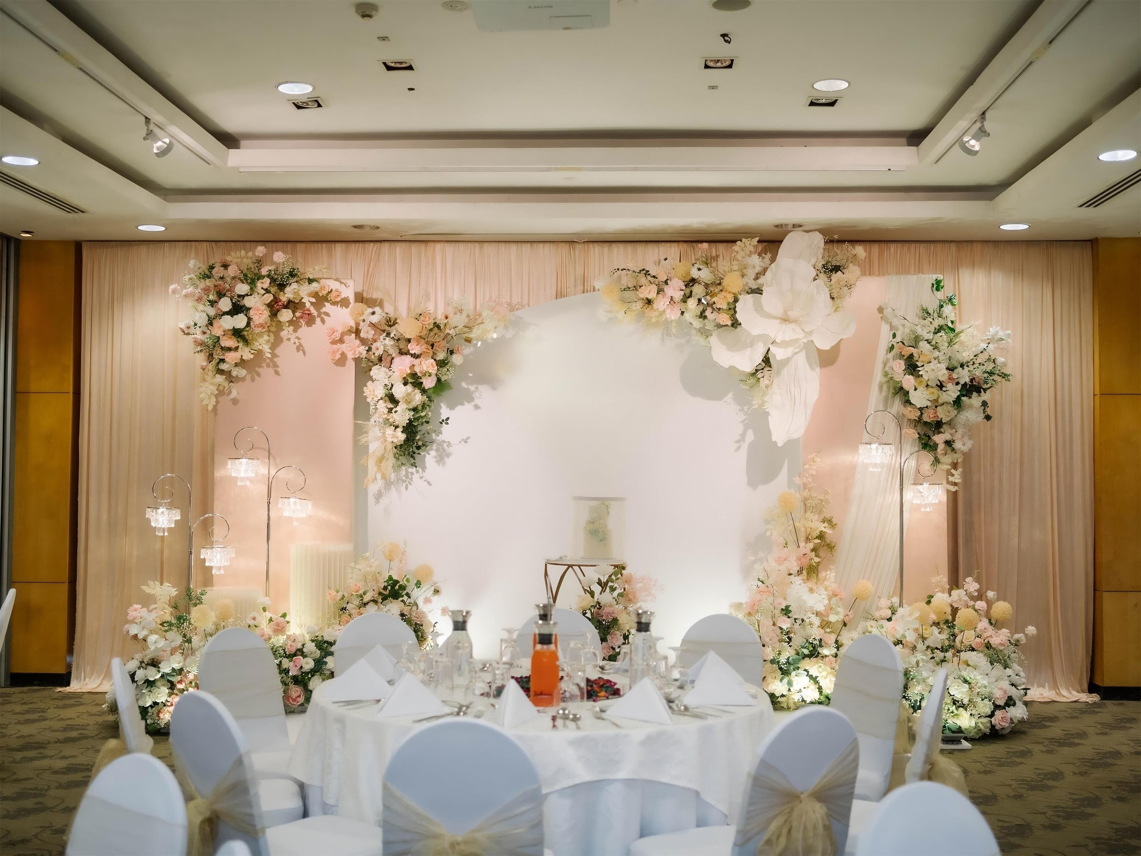 A banquet hall with round tables set for a formal event, adorned with floral arrangements and white tablecloths.