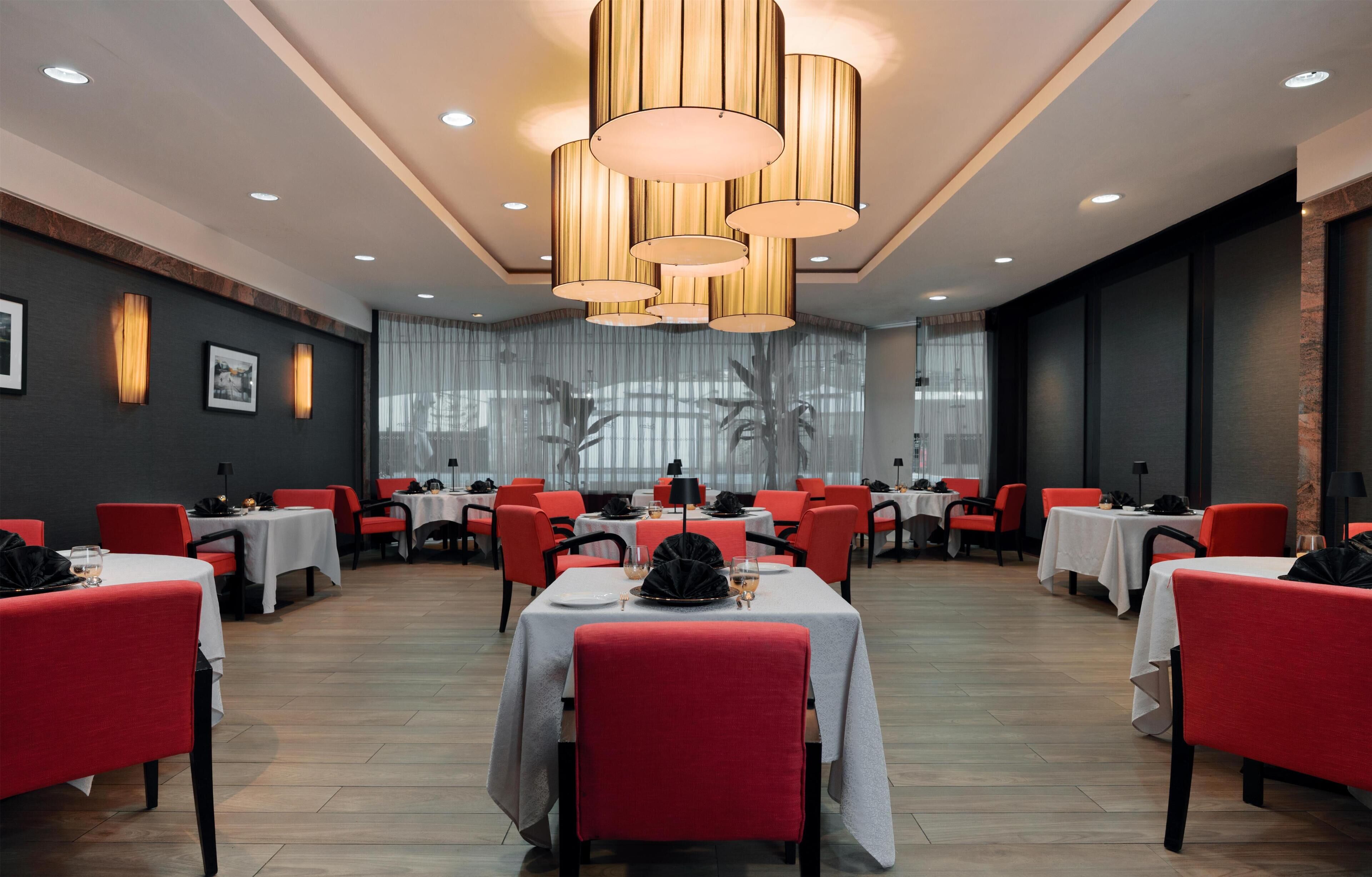 Un ristorante con diversi tavoli e sedie, un lampadario e un'ampia finestra con tende.