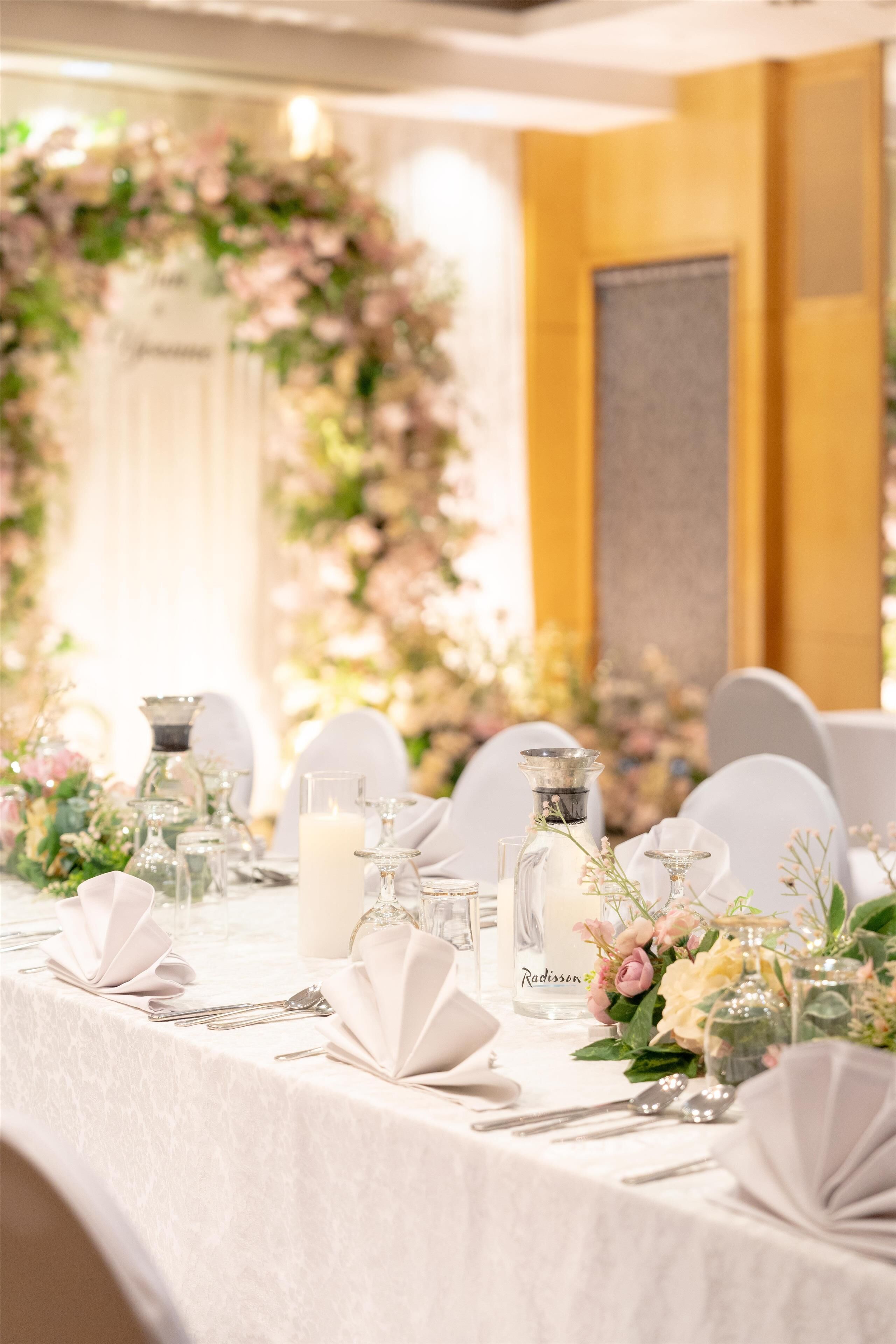 Mesa dispuesta para un evento formal, con manteles blancos, cristalería y centros de mesa florales.