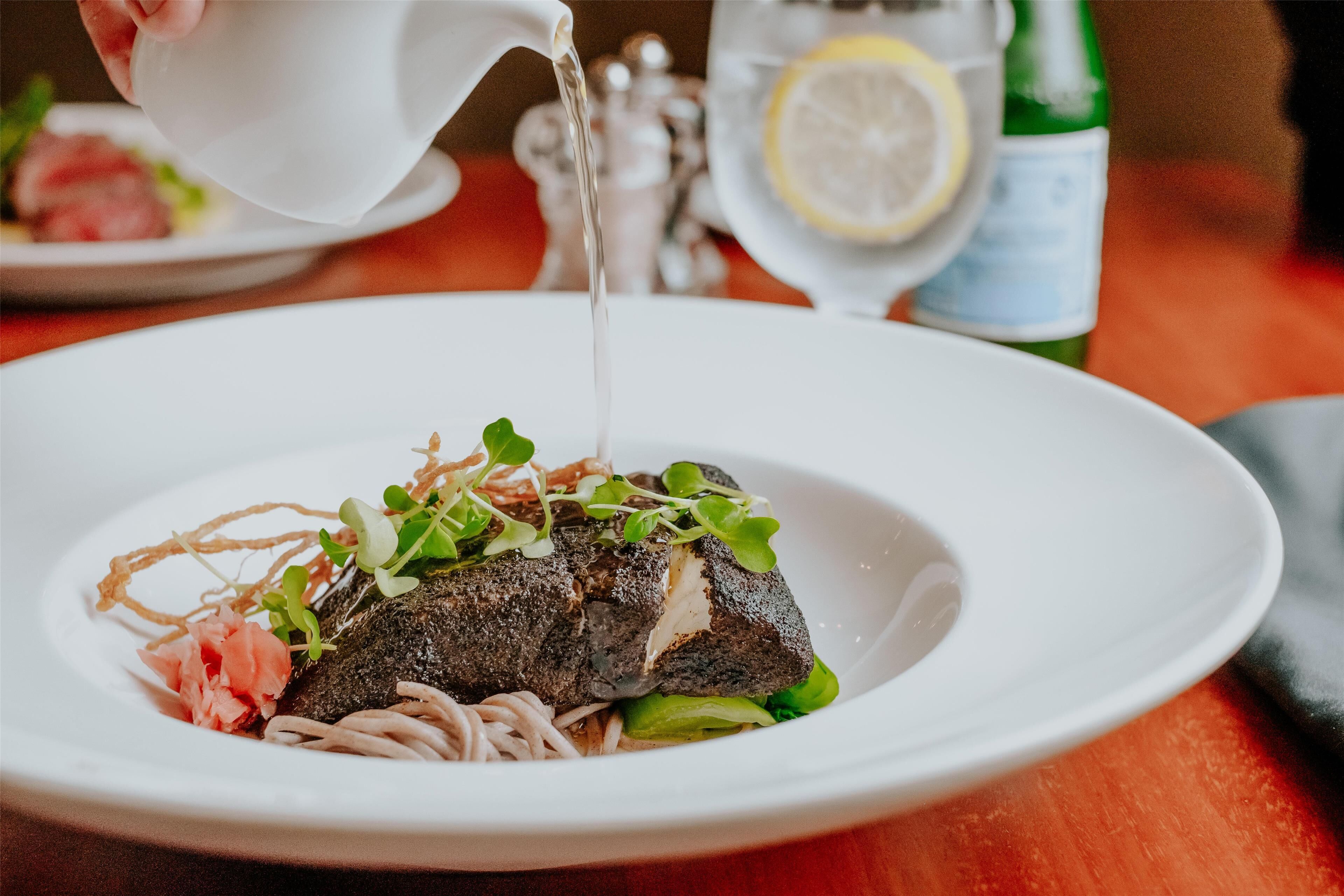 Une assiette blanche contenant un plat de poisson, agrémenté de verdure et de saumon rose, posée sur une table en bois.